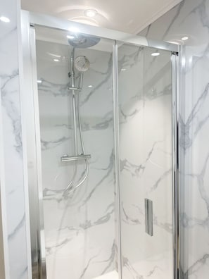 A modern shower enclosure with a glass door and a marble-patterned wall. - Cozy 1BR & Living Room Near City Center (Ghent)