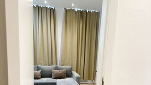 Un salon moderne avec un canapé d’angle gris, un petit pouf et un tapis de couleur claire.