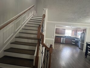 Eine Treppe mit Holzhandläufen und einer Zwischenebene, die zu einer Küche mit Holzausstattung und Edelstahlgeräten führt.