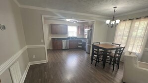 Un'ampia zona giorno con parquet, un tavolo da pranzo con sedie, un divano e una cucina sullo sfondo.