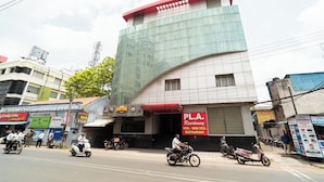 A multi-story building with a modern glass facade, a red sign for 'PL.A. Residency' indicating a restaurant, and several motorcycles parked in front. - PLA Residency Tanjore (Thanjavur)