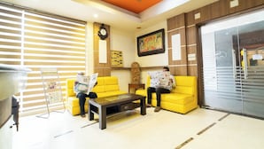 A reception area with two yellow sofas, a coffee table, a clock, a framed picture, and a glass door. - PLA Residency Tanjore (Thanjavur)