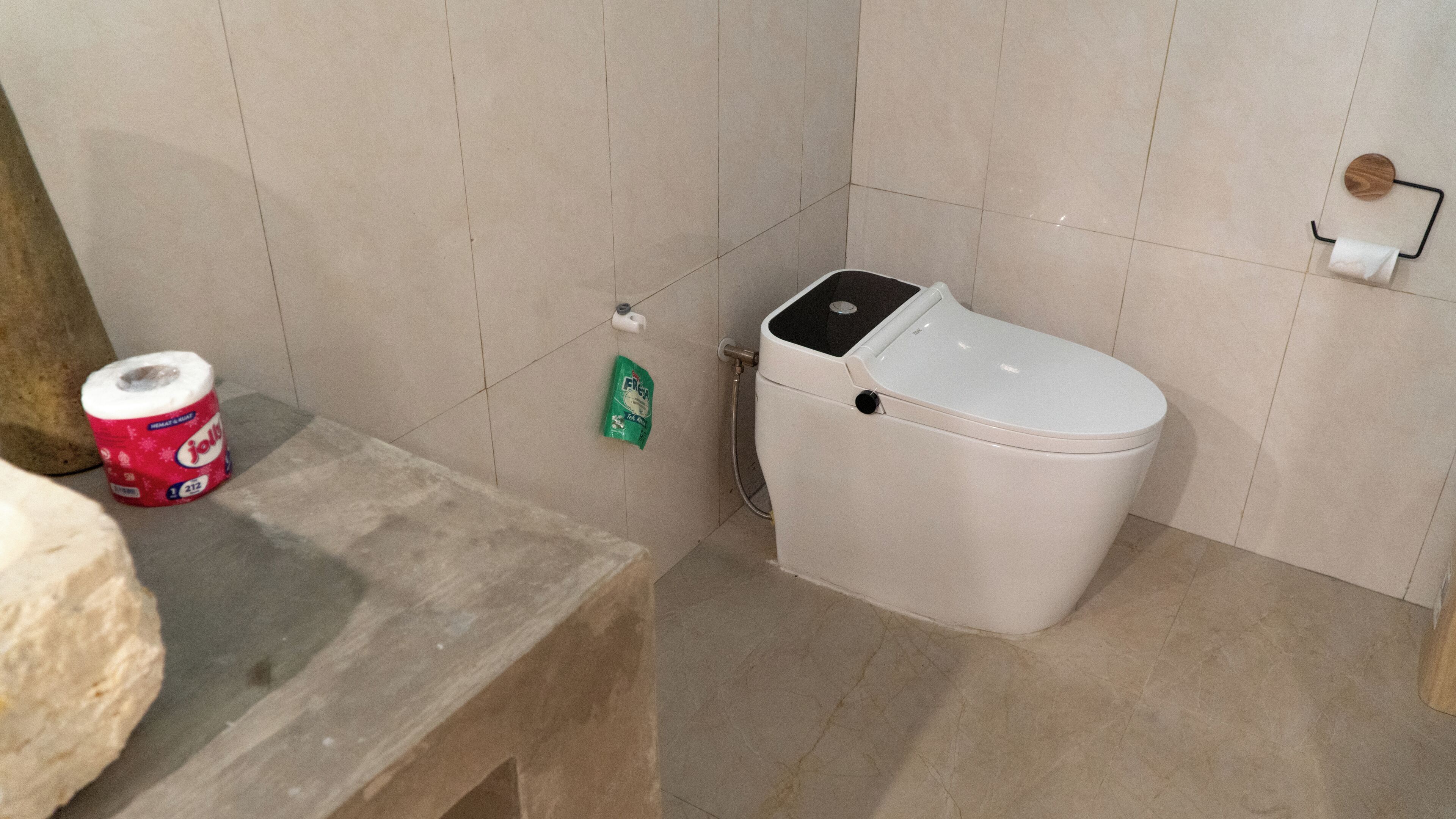 Un baño con un inodoro, un rollo de papel higiénico y un pequeño cubo de basura.