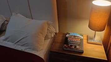 Een hotelkamer met een bed, kussens, een nachtkastje, een boek getiteld 'BOROBUDUR Trail of Civilization' en een lamp.
