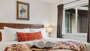 A hotel room with a bed, a framed picture on the wall, a window with curtains, and a bedside lamp. - Family Stay Central To Glacier + Whitefish (Columbia Falls)