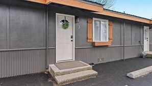A two-story building with a grey exterior, a white front door with a wreath, and a small window with wooden shutters. - Family Stay Central To Glacier + Whitefish (Columbia Falls)
