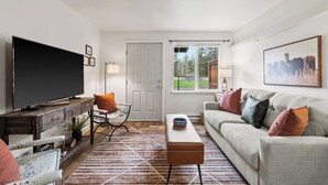 A living room with a TV, sofa, coffee table, and a door leading to a balcony. - Family Stay Central To Glacier + Whitefish (Columbia Falls)