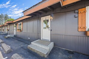 Une rangée de bâtiments de style motel, chacun ayant une seule porte d’entrée, des marches menant à la porte et un petit espace porche agrémenté de jardinières.