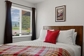 Une chambre à coucher avec un lit, une fenêtre avec des rideaux, une tête de lit et un tableau encadré au mur.