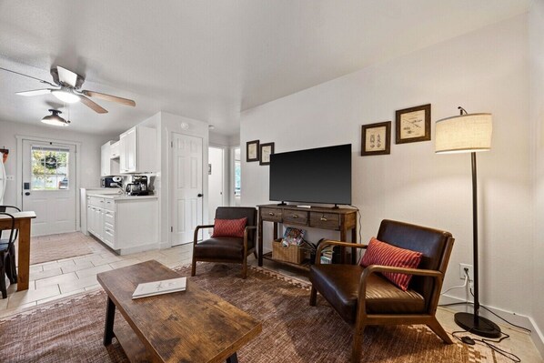 Un salon avec un téléviseur, deux fauteuils, une table basse et un lampadaire.