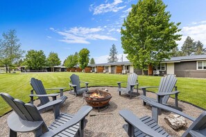 Uma lareira com cadeiras Adirondack, um gramado bem cuidado e uma fileira de cabanas ao fundo.