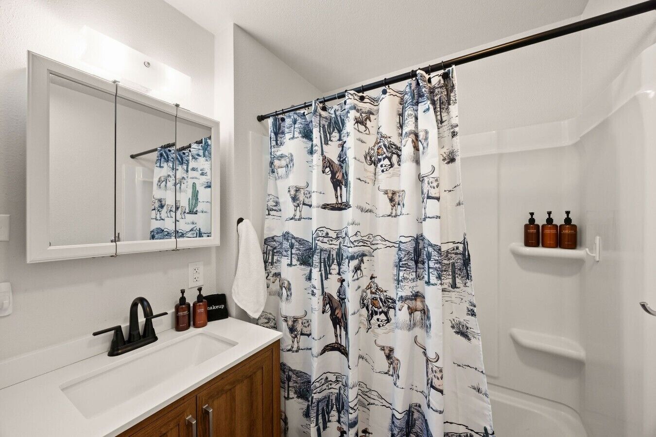 Een badkamer met een douchegordijn met dierenprints, een spiegel, een wastafel met toiletartikelen en een handdoekhouder.