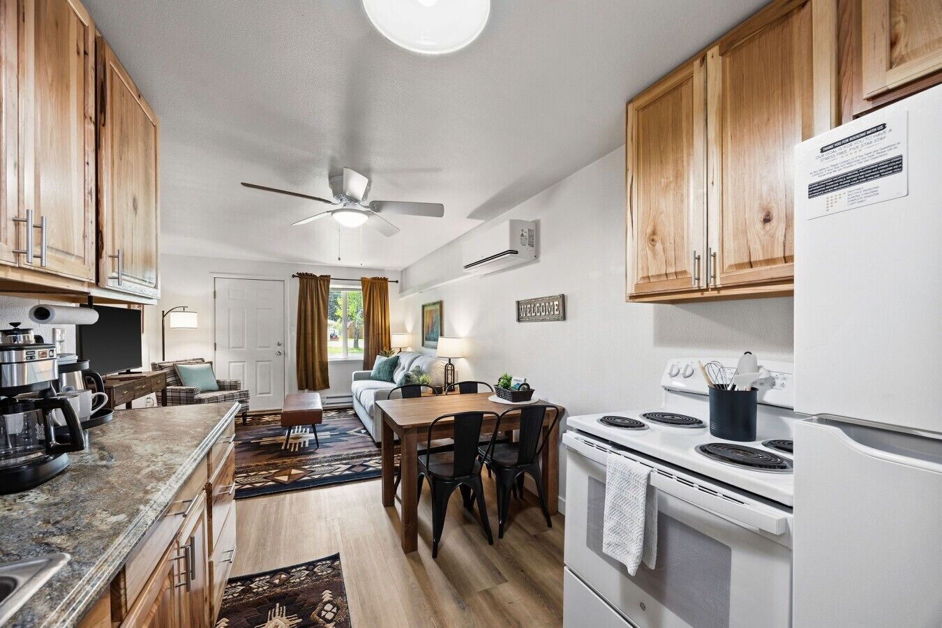 A compact kitchen with wooden cabinets, a white stove, and a dining area with a table and chairs.
