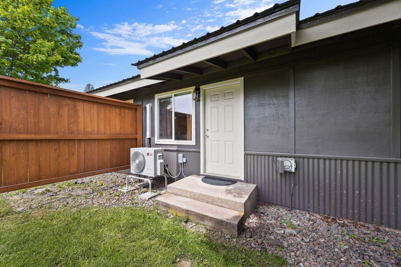 A residential building with a wooden fence, a white door, an air conditioning unit, and a small concrete step leading to the entrance.