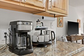Una cocina con cafetera, tazas y televisor.
