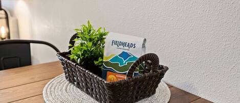 Een rieten mand met een koffiezakje en een plantje op een ronde geweven onderzetter op een houten tafel.