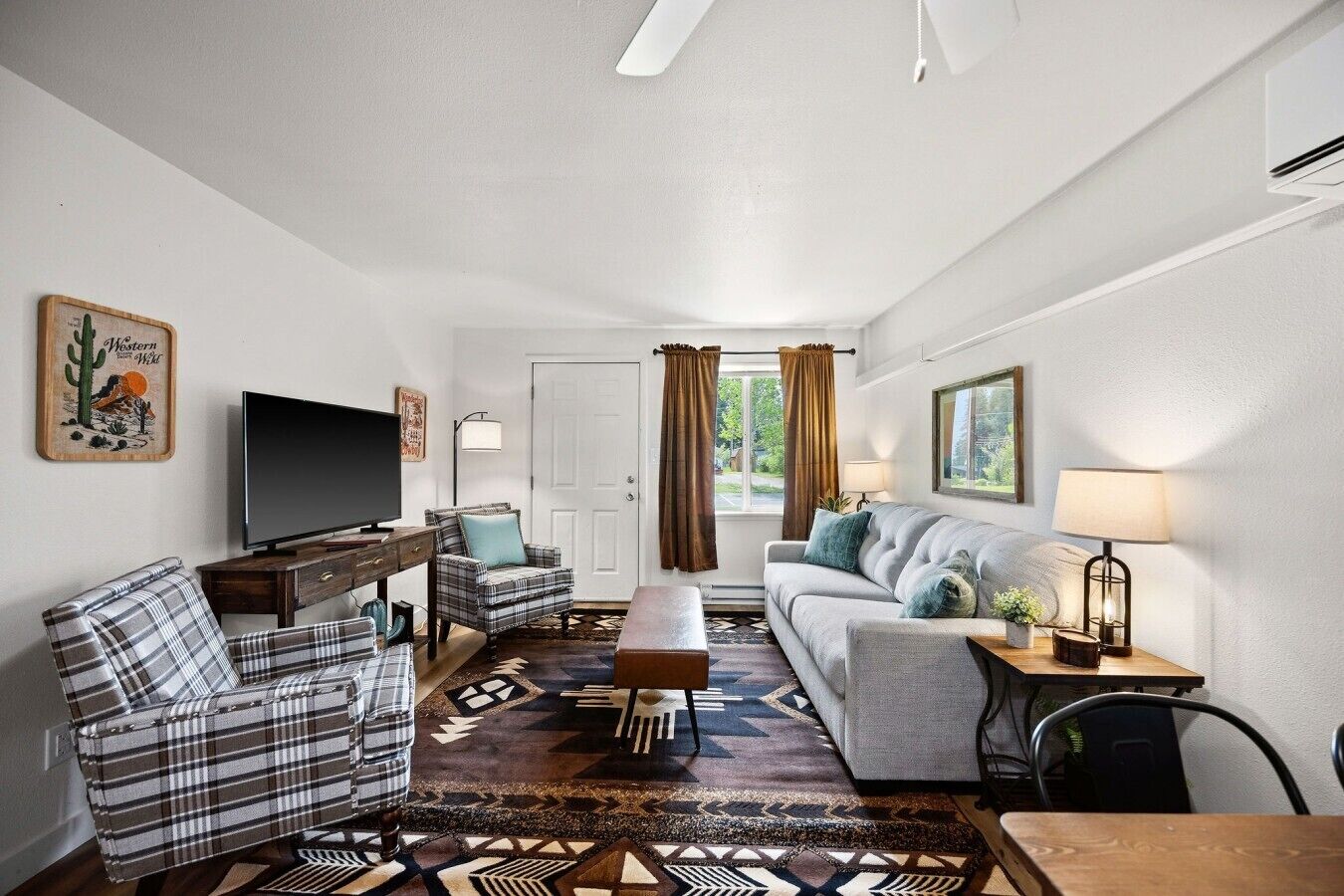 Ein Wohnzimmer mit Sofa, Sessel, Fernseher und einem gemusterten Teppich.