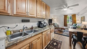 A kitchen with wooden cabinets, a granite countertop, a coffee maker, and a dining area with a table and chairs. - Family Stay Near Glacier + Whitefish w/ Pickleball (Columbia Falls)
