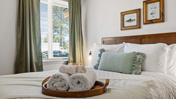 A neatly made bed with rolled towels, a wooden headboard, and two framed pictures on the wall. - Glacier NP Retreat w/ Modern Comforts & Pickleball (Columbia Falls)