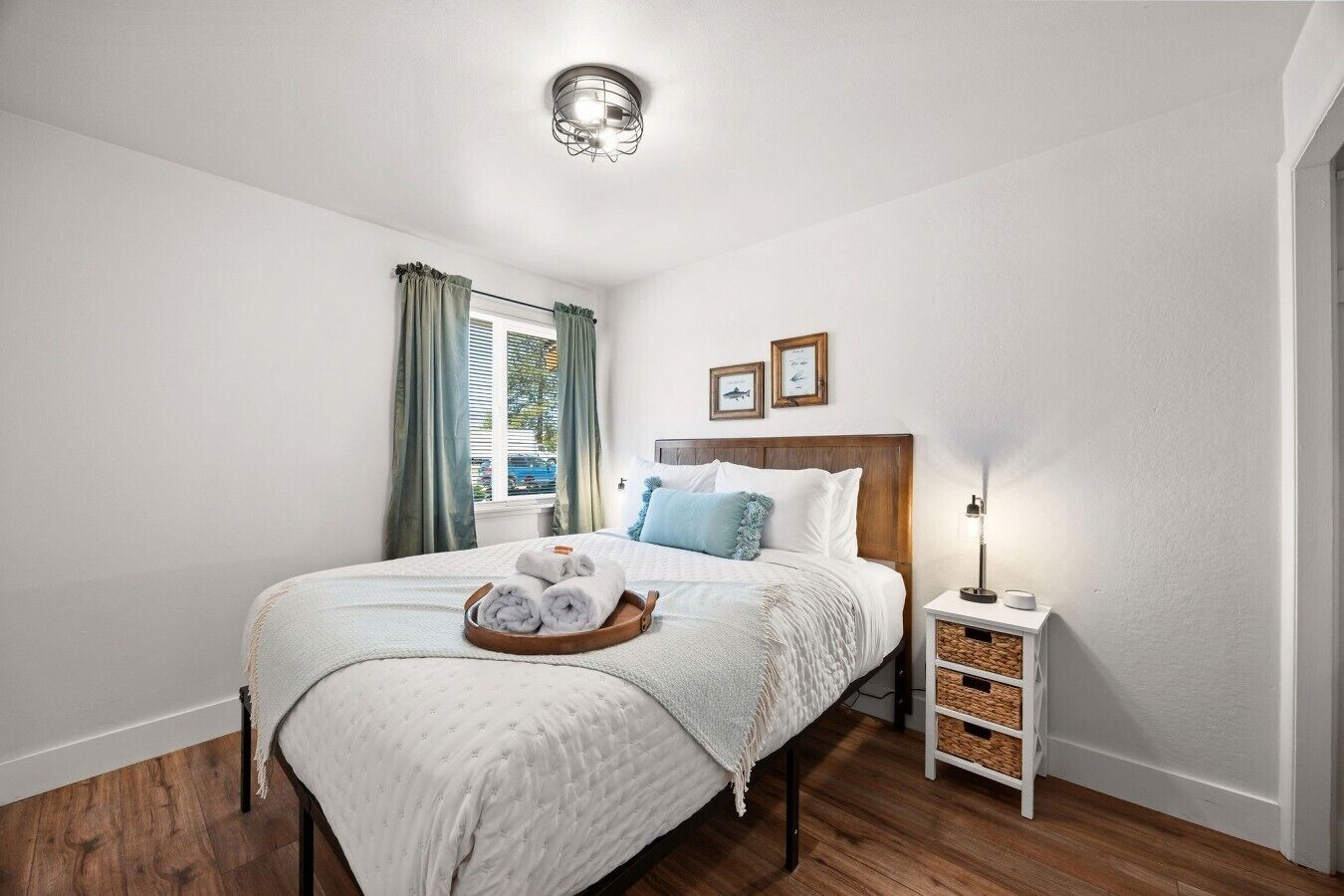 A neatly arranged bedroom with a bed, a bedside table, a lamp, and a window with curtains.