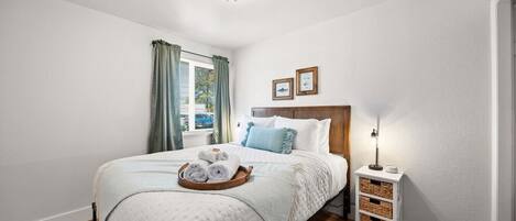 A neatly arranged bedroom with a bed, a bedside table, a lamp, and a window with curtains.