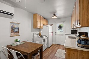 Une cuisine compacte avec des meubles en bois, un poêle blanc, un réfrigérateur et une table à manger avec des chaises.