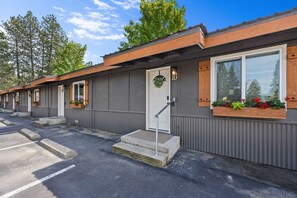 A row of single-story mobile homes with a grey exterior, wooden window frames, and a front door with a small porch.