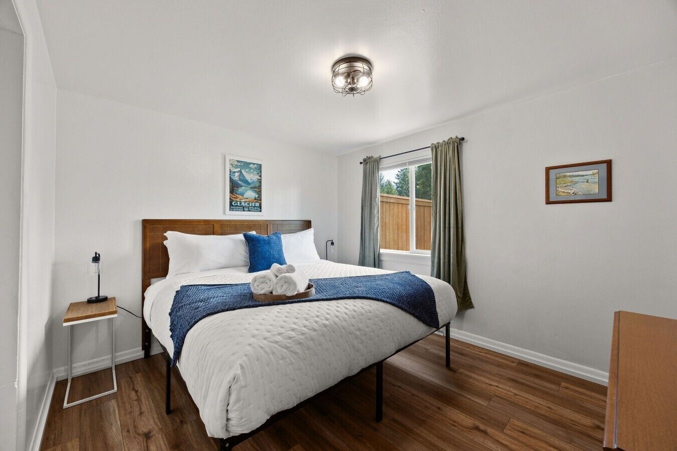 A neatly arranged bedroom with a wooden bed frame, a bedside table with a lamp, and a window with curtains.