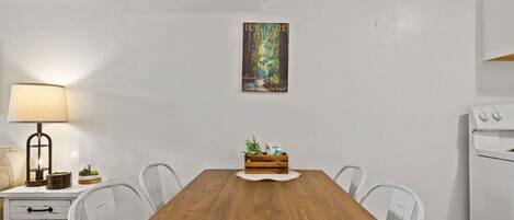 A dining area with a wooden table, chairs, a lamp, a small plant, and a framed picture on the wall.