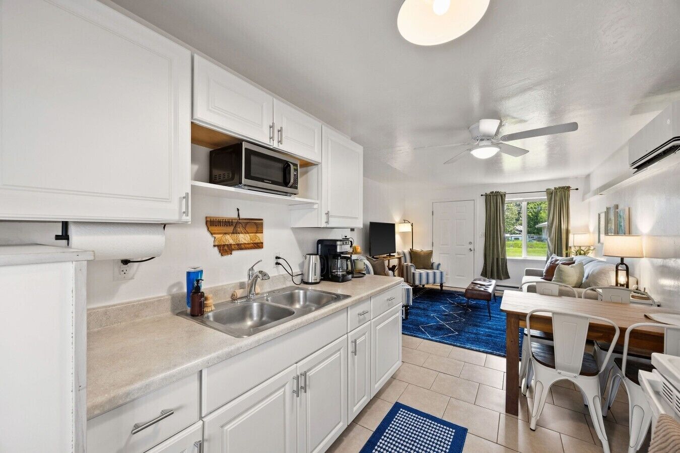 A compact kitchen with a microwave, sink, and coffee maker. There is a dining area with a table and chairs.