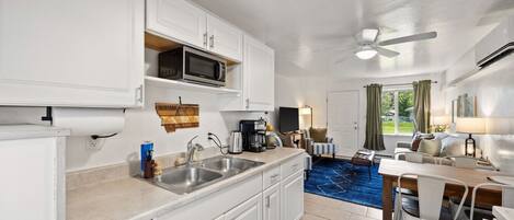 A compact kitchen with a microwave, sink, and coffee maker. There is a dining area with a table and chairs.