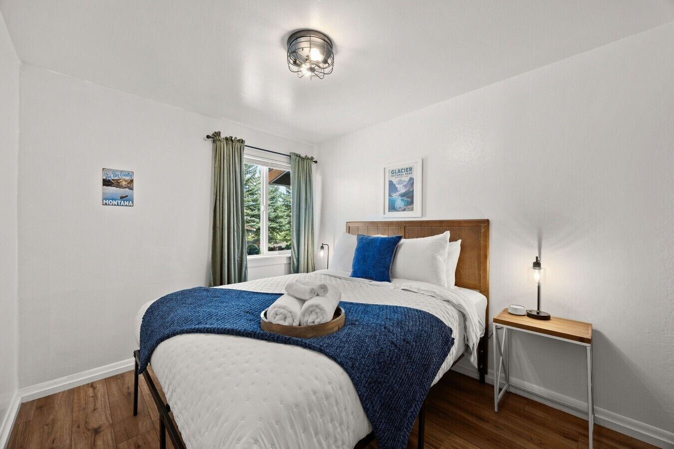Ein ordentlich eingerichtetes Schlafzimmer mit Bett, Nachttisch, Lampe und einem Fenster mit Vorhängen.