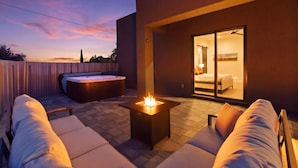 Un patio exterior moderno con una chimenea, un jacuzzi y una puerta de cristal que da a un dormitorio.