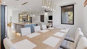 Un comedor moderno con una larga mesa de madera, sillas blancas e iluminación colgante.