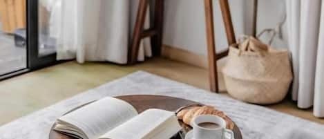 A cozy reading nook with a round wooden table, a book, a cup of coffee, and a croissant.