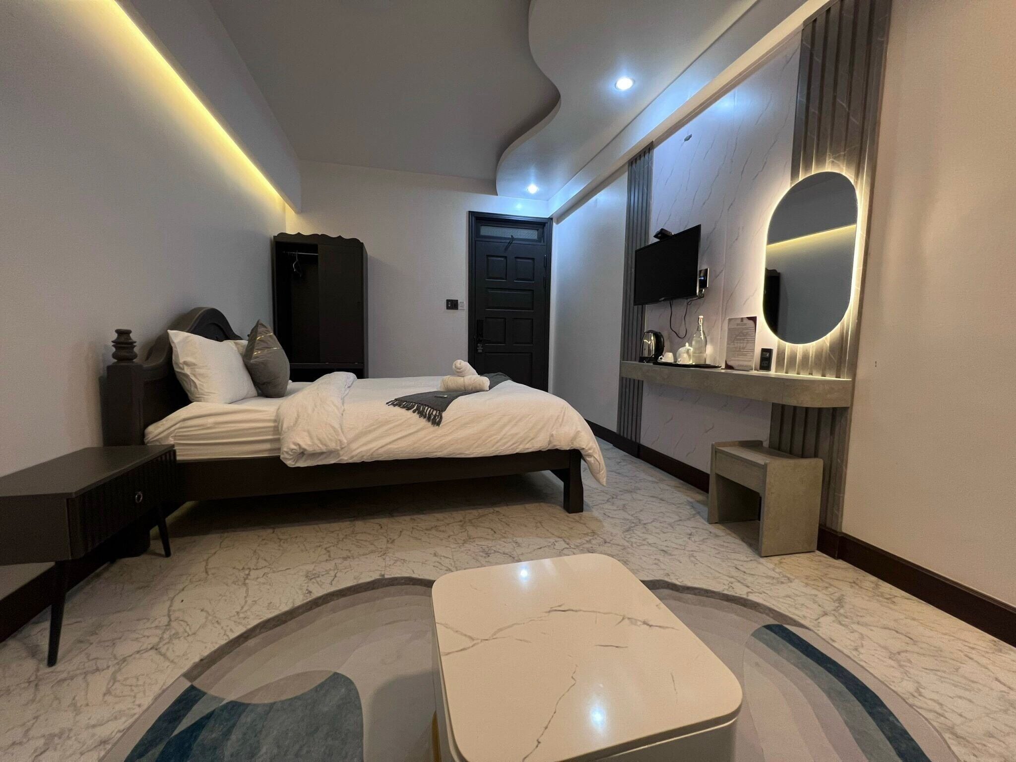 Quarto moderno com cama, mesas de cabeceira, espelho e chão de mármore.