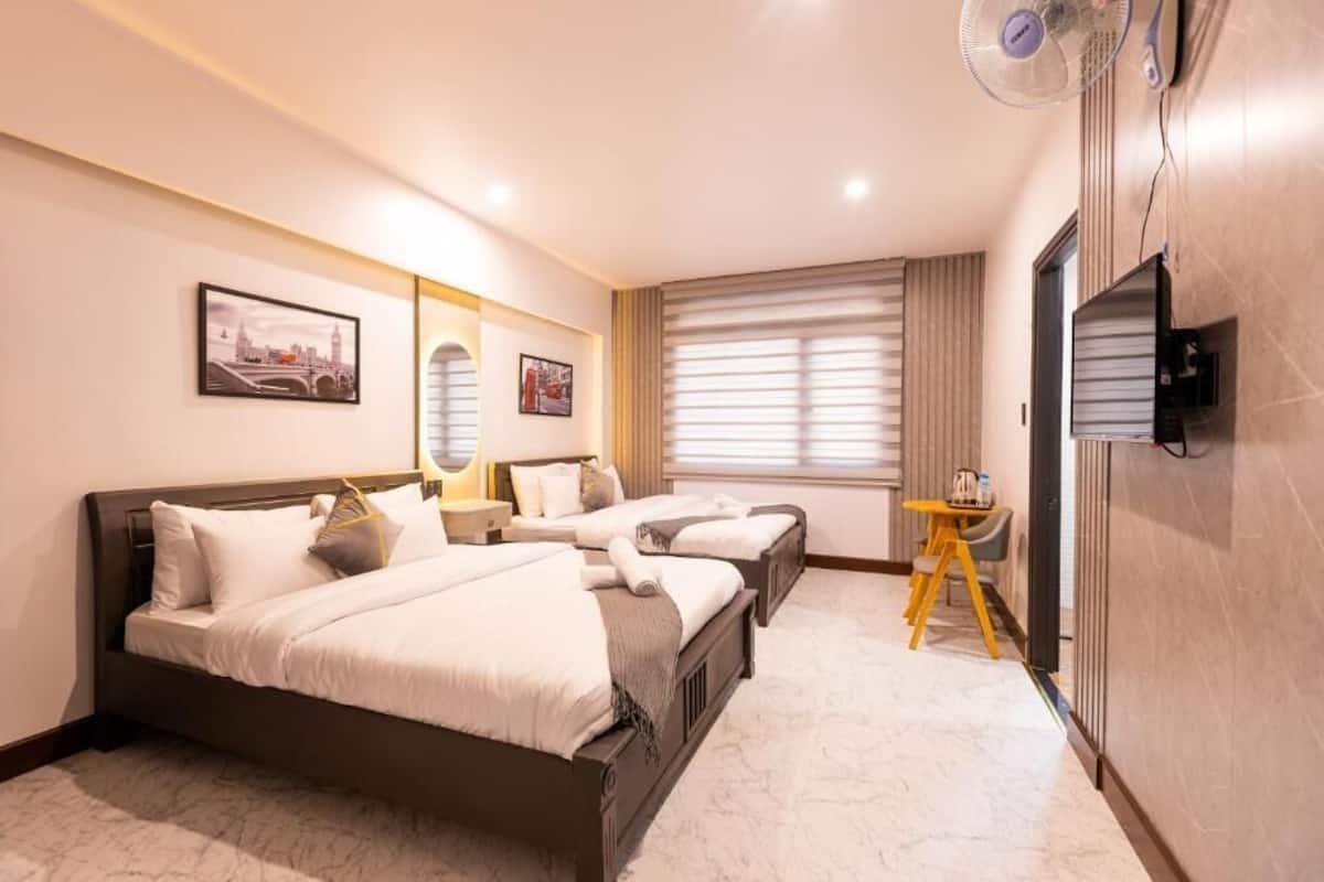 Habitación de hotel con dos camas, un televisor, un ventilador y una mesita.
