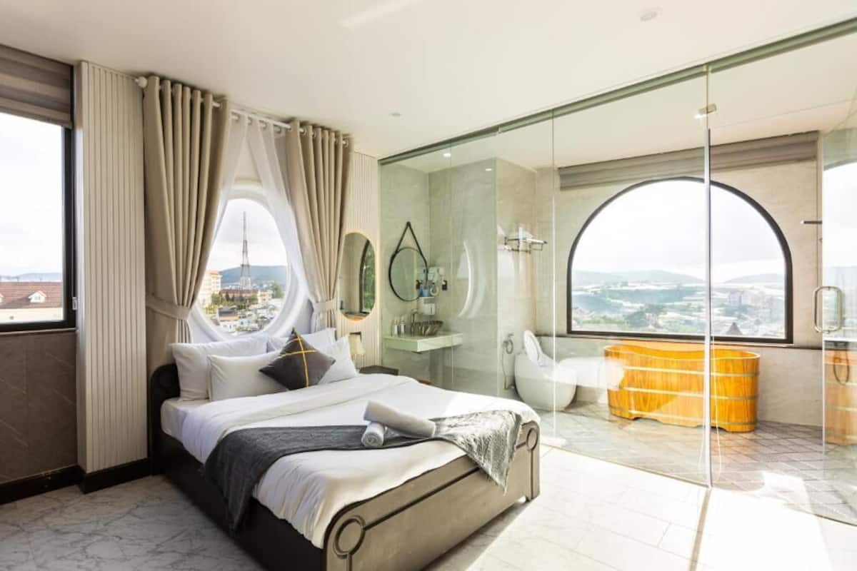 Una habitación de hotel moderna con una cama grande, cabina de ducha de vidrio, vistas a la ciudad y una bañera.