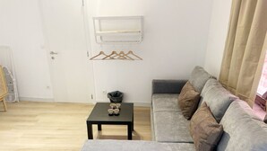 A living room with a grey sofa, a small table with cups, a coat rack, and a white door. - Convenient Studio in the Heart of City (Ghent)