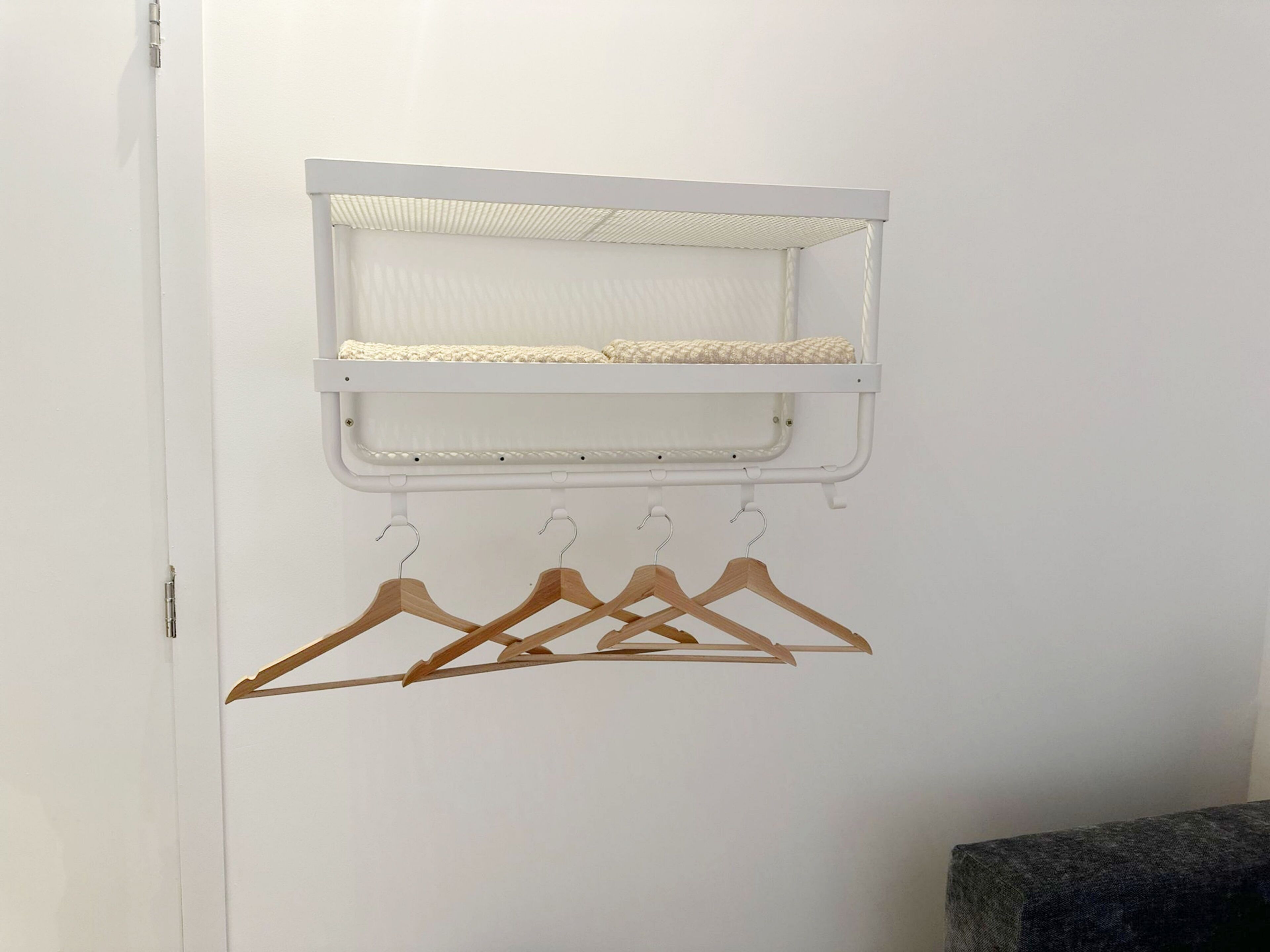 A white wall with a white shelf above a set of wooden hangers.