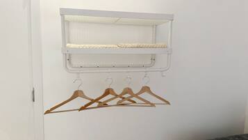 A white wall with a white shelf above a set of wooden hangers.