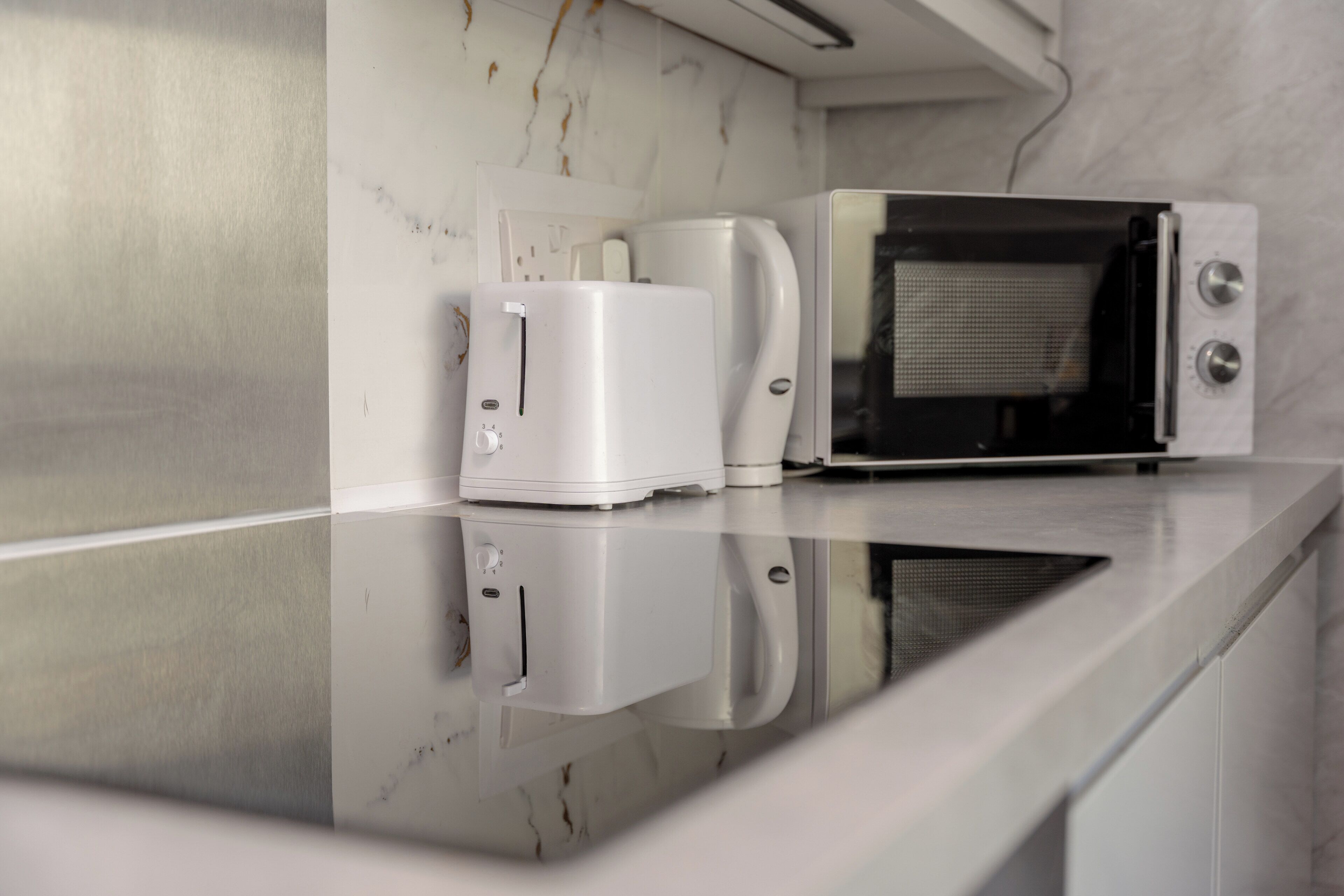 A kitchen with a modern design, featuring a white countertop, a coffee maker, and a microwave.