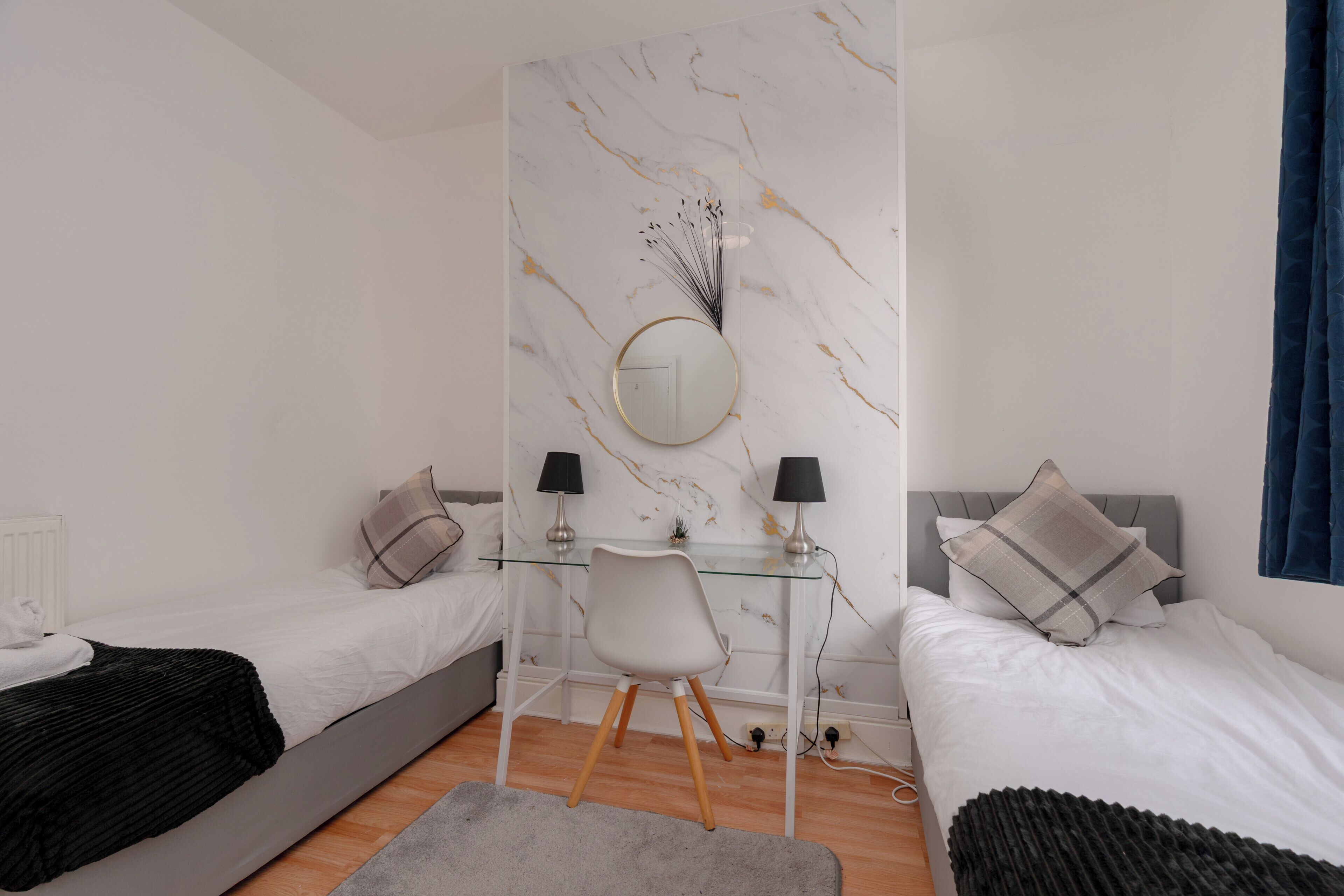 Ein Schlafzimmer mit zwei Betten, einem Schreibtisch, einem Sessel, einem runden Spiegel und einer Wand mit Marmoroptik.