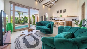 A spacious living area with a large sliding glass door leading to a balcony, a kitchen in the background, and a ceiling fan. - La Palma Villa Bali (Kerobokan)