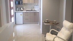 A compact kitchen with a microwave, kettle, and small refrigerator. There is a dining area with a chair and table, and a glass partition separates the kitchen from the living space. - Apartment in the heart of Bondi (Bondi)