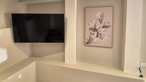 A room with a flat-screen TV mounted on the wall, a framed floral artwork, and a white shelf. - Apartment in the heart of Bondi (Bondi)