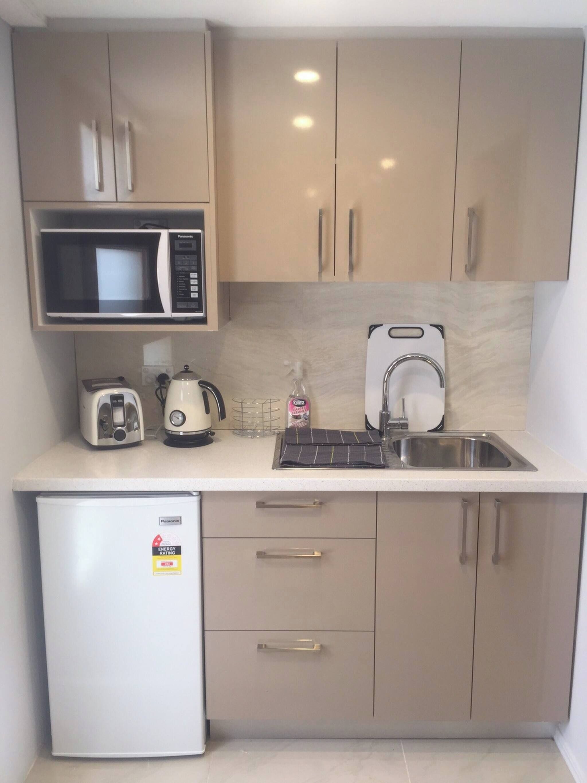 A compact kitchenette with a microwave, toaster, kettle, and a small refrigerator.
