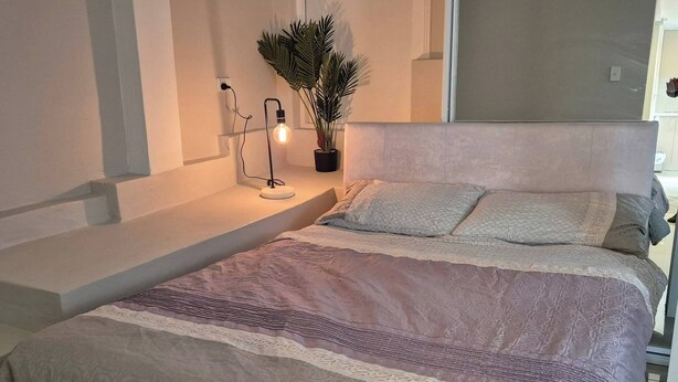 A bedroom with a bed, a nightstand, a lamp, and a potted plant. - Apartment in the heart of Bondi (Bondi)