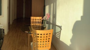 A dining area with a glass table and wooden chairs, a vase with flowers, and a shadow on the wall. - Cosy Apartment with great Wi-Fi, City Centre (Nottingham)