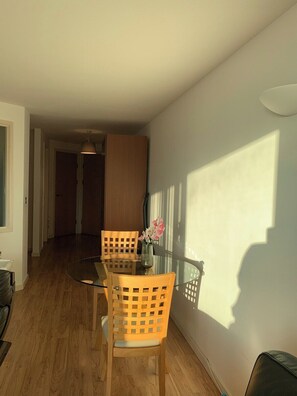Ein Essbereich mit einem Glastisch und Holzstühlen, einer Vase mit Blumen und einem Schatten an der Wand.